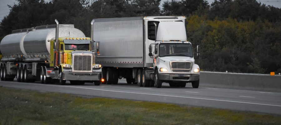 trailer-trucks-driving-road-surrounded-by-beautiful-green-trees-min